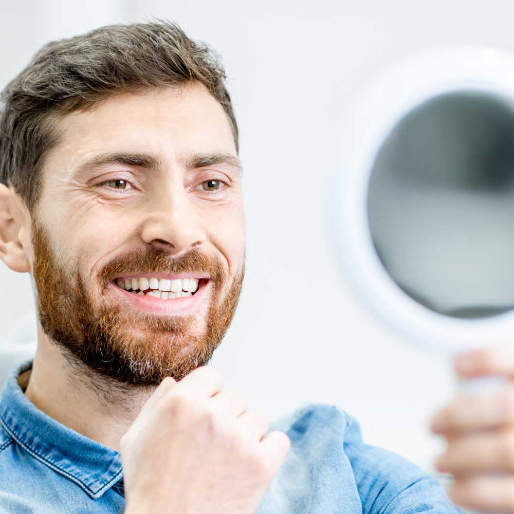 man looking at his nice teeth with partial in a mirror